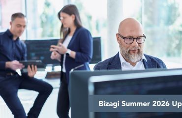 SITS-bizagi-summer-update Foreground: man with glasses at a computer in a bright office, two coworkers collaborate in the background, banner reads 'Bizagi Summer 2026 Update'.
