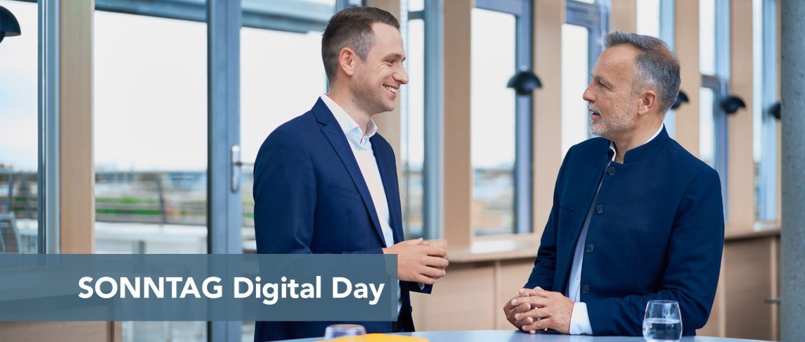 Two men in navy suits chat in a bright, modern space; a blue banner across the bottom reads 'SONNTAG Digital Day'