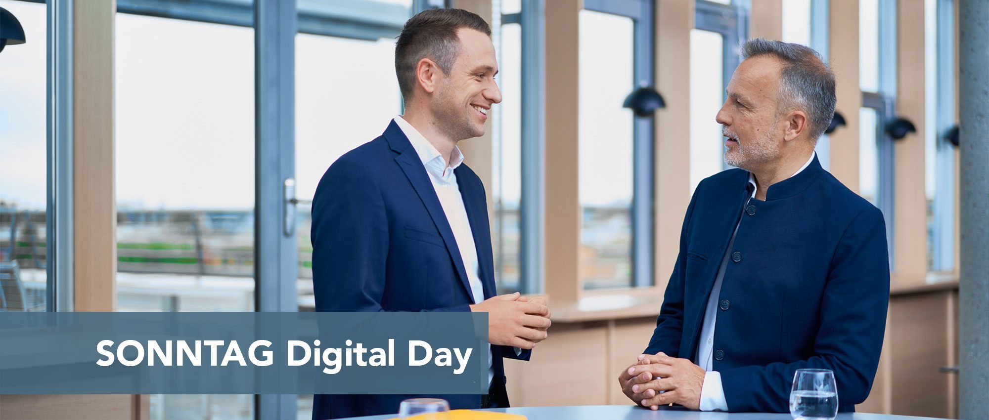 Two men in navy suits chat in a bright, modern space; a blue banner across the bottom reads 'SONNTAG Digital Day'